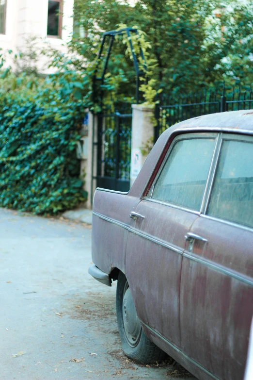 a maroon car parked on the street near some hedges