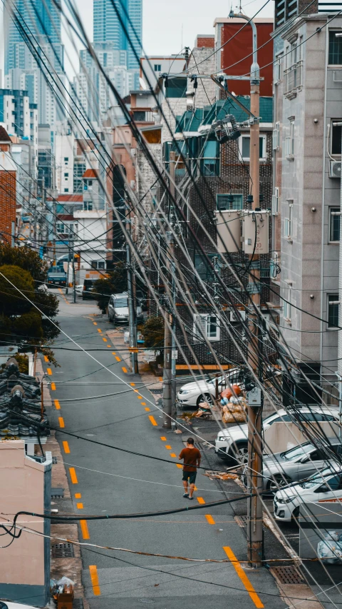 a man walking down the street with cars and wires above him