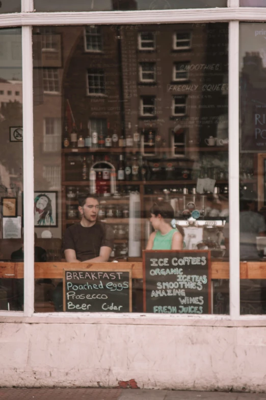 two men sit at a table behind a cafe window