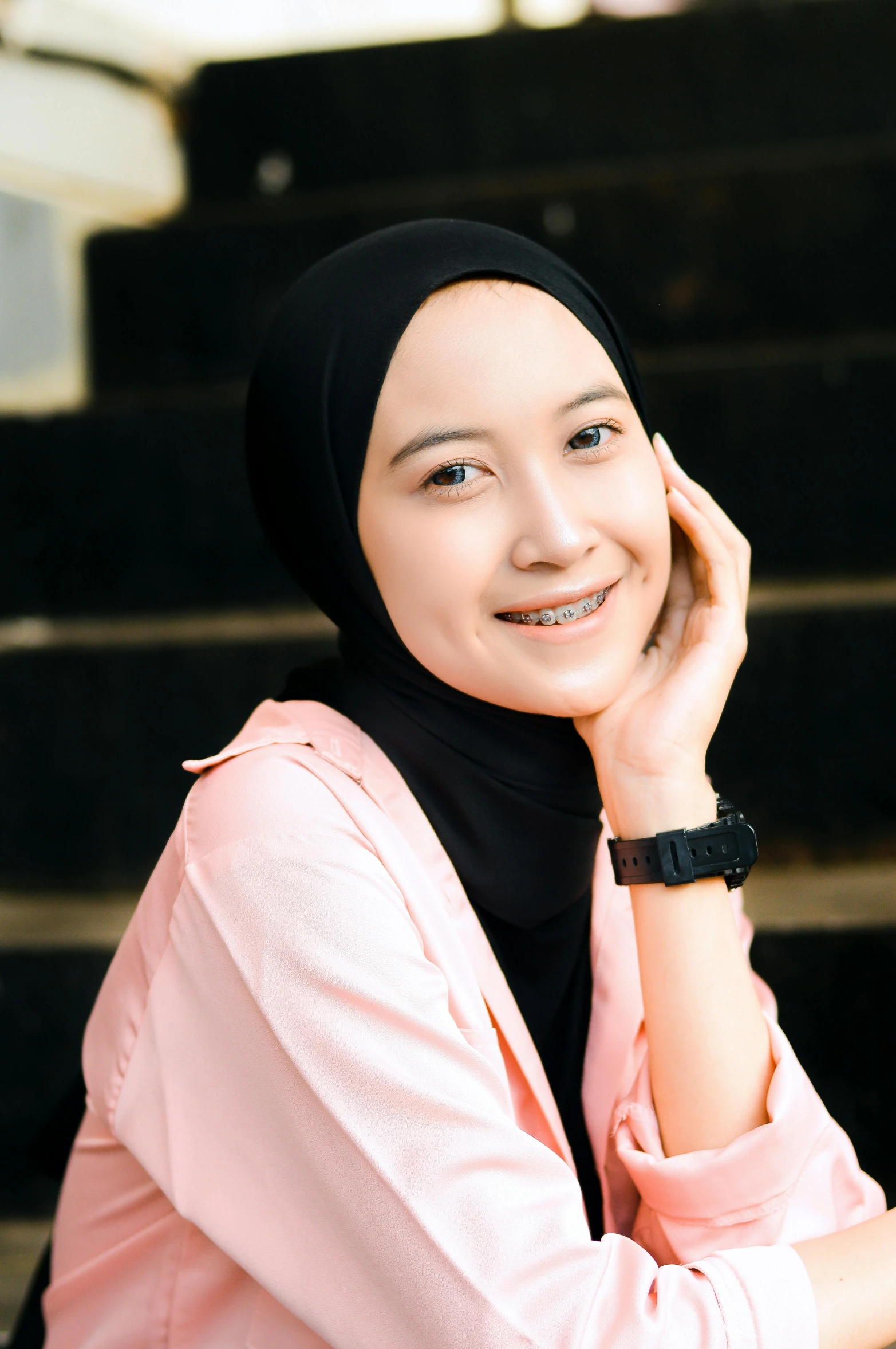 a woman wearing a hijab and smiling while sitting on some steps