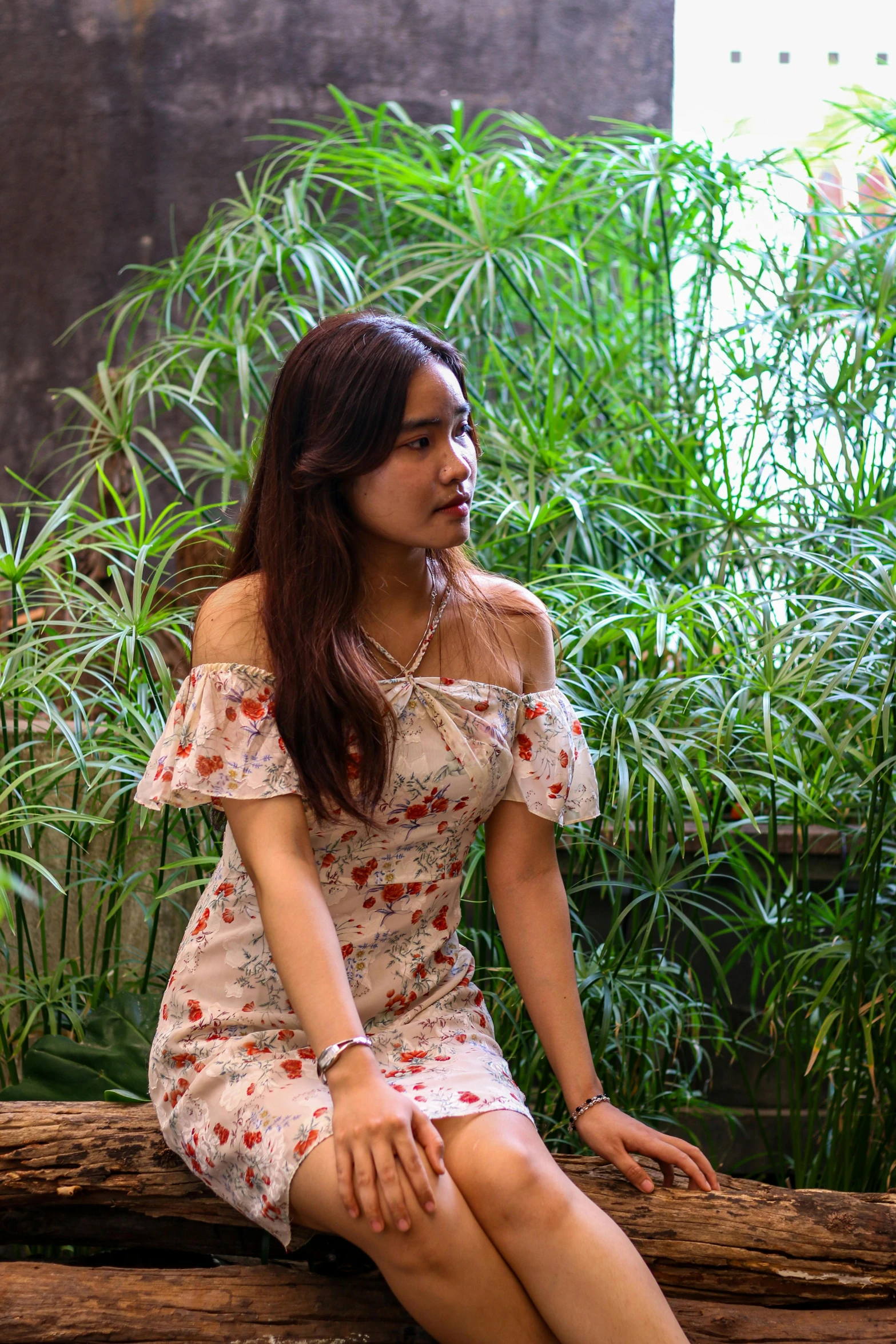 asian girl sitting on log near greenery