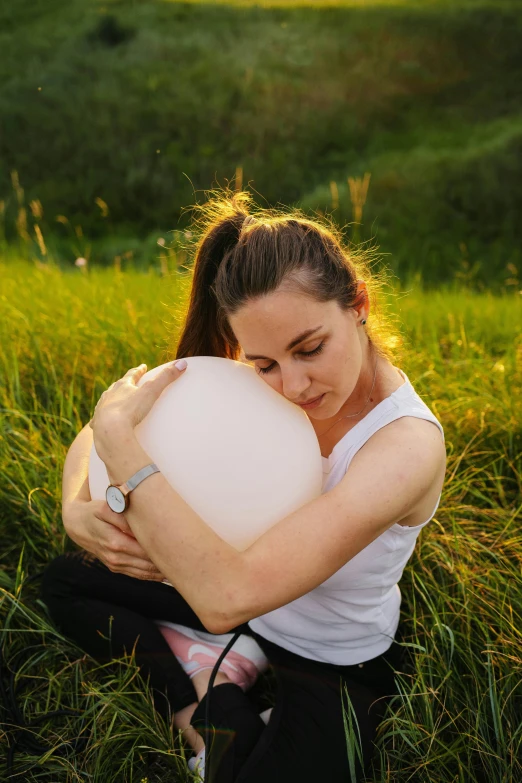 woman kneeling in grassy field while holding onto an oversized white object