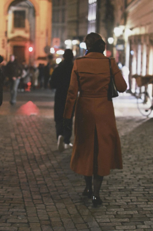 a woman wearing a trench coat walking on a cobblestone street