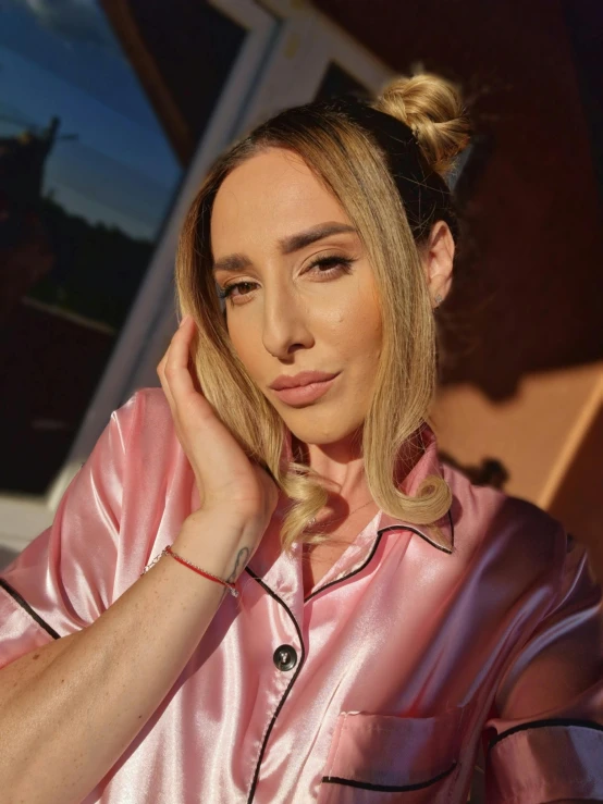 a woman wearing a pink pajama sits in front of an open window