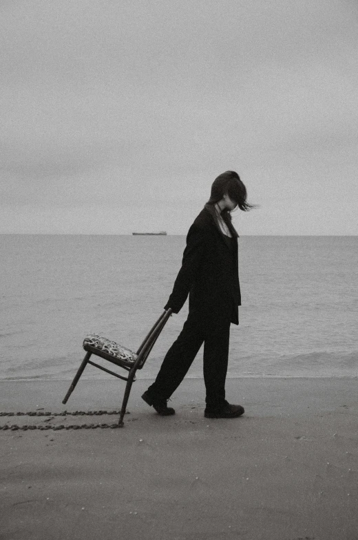 a woman walking on the beach with a chair to her face