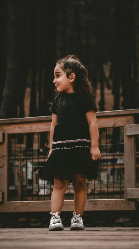 a little girl in a dress standing on the edge of a deck