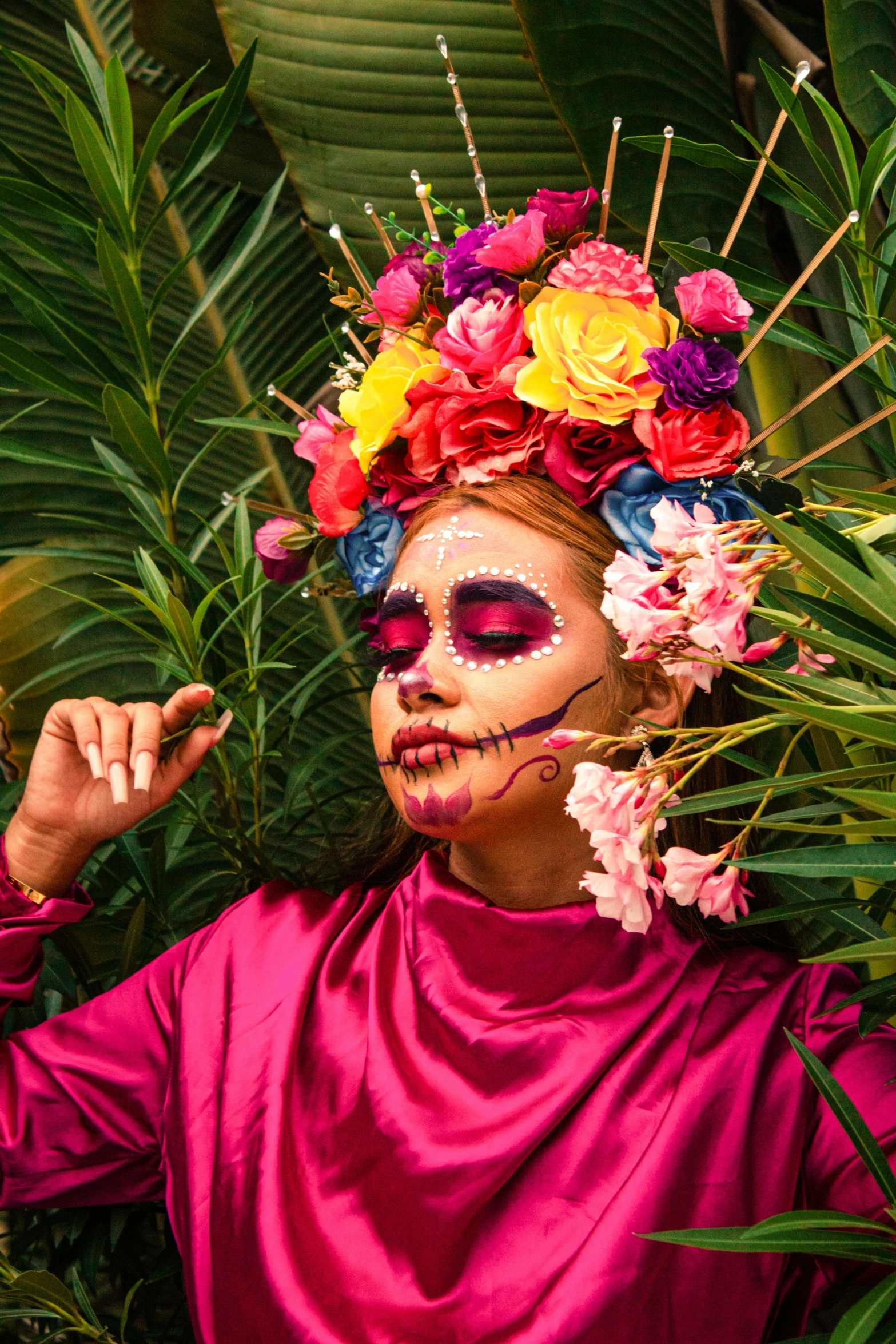 a person in a pink shirt and flower head dress standing in a lush green area