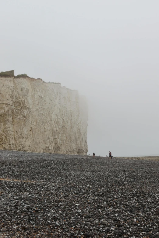 two people are standing on rocks by the side of the beach with a large cliff in the background