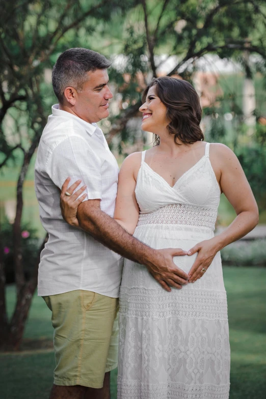 a pregnant couple standing next to each other in the grass