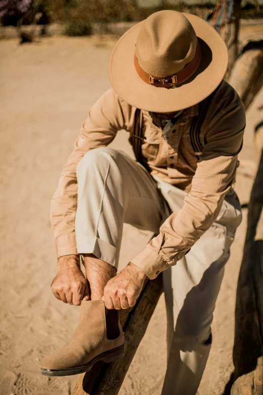 a man leaning on a fence wearing a hat and boots