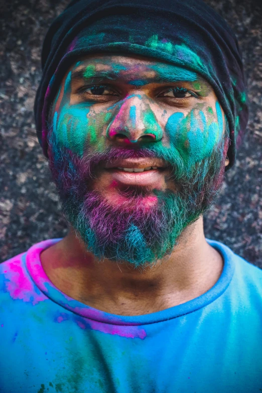 a man in a blue shirt and a purple hat with green and pink paint on his face