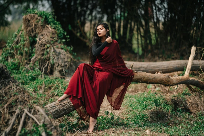 a woman sits on a tree log in a dress