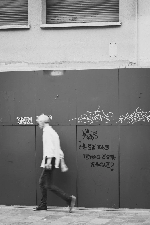 a man walks past some graffiti writing on a wall
