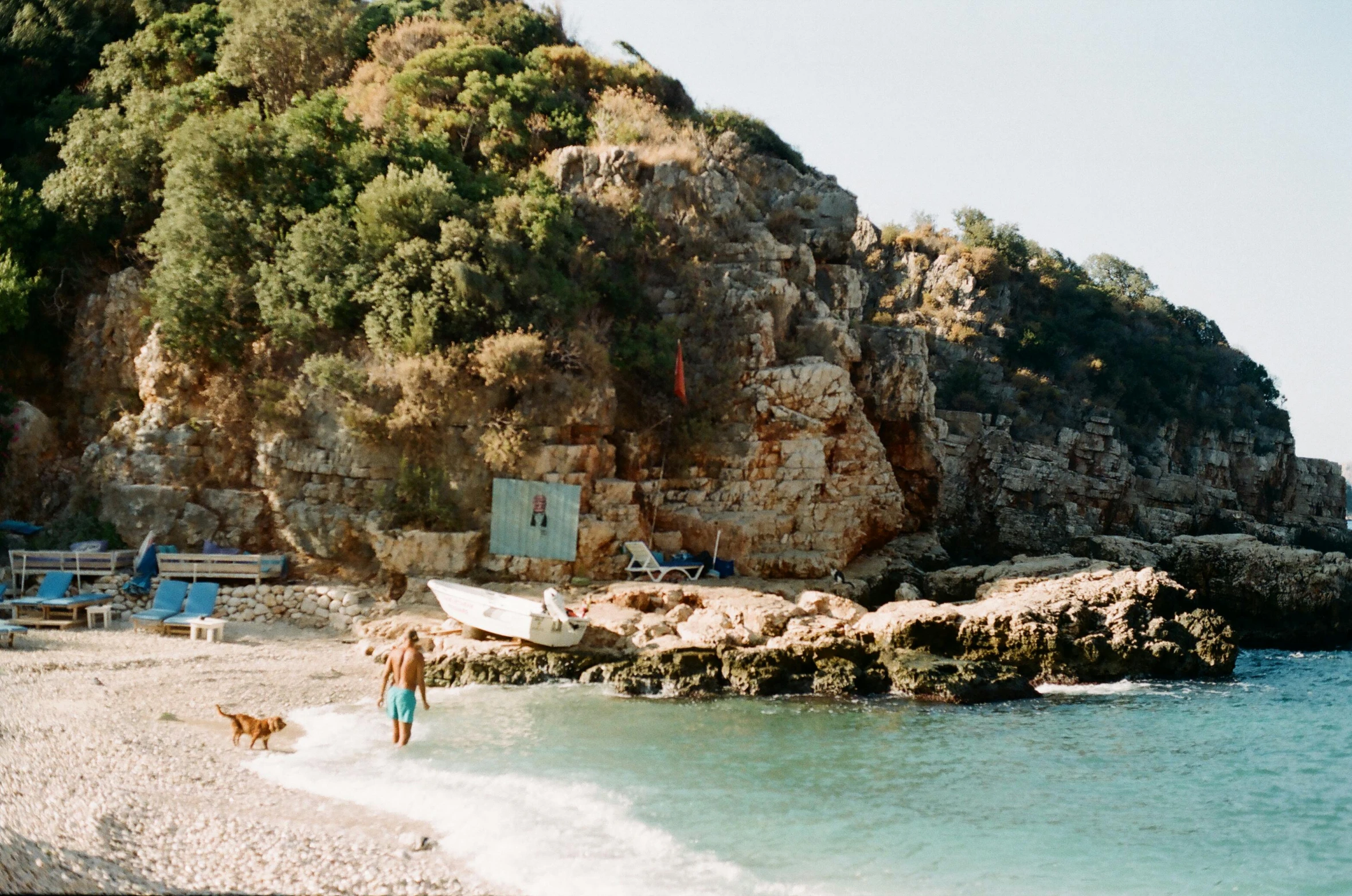 a person and a dog on the beach near a large rock cliff