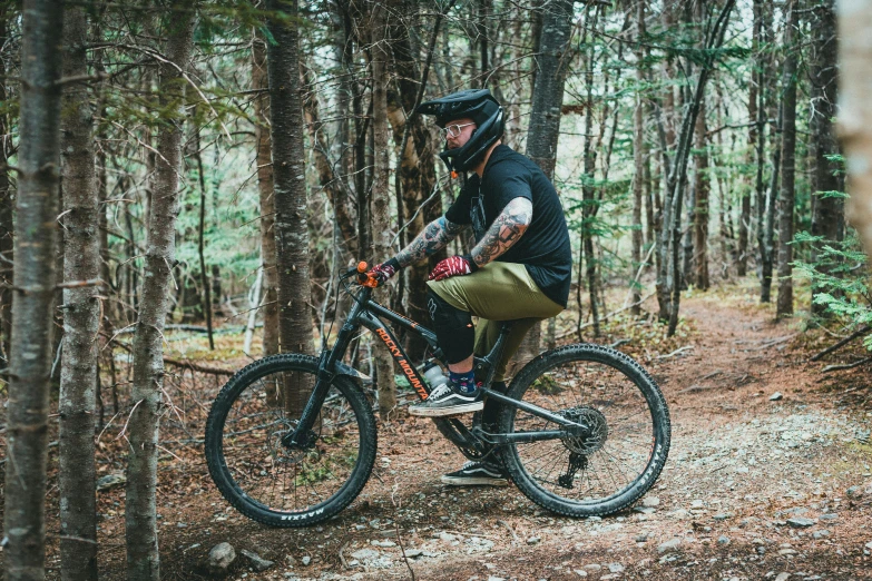 a man with tattoos on riding a bicycle through the woods