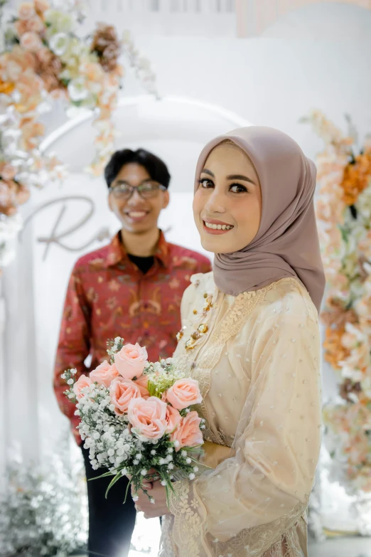 young asian couple smiling and holding flowers under archway