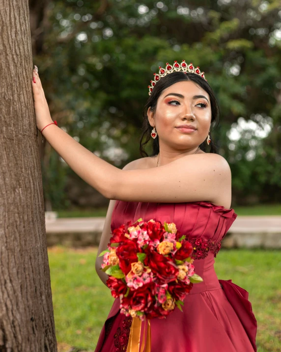 the girl is standing against a tree holding a bouquet of flowers