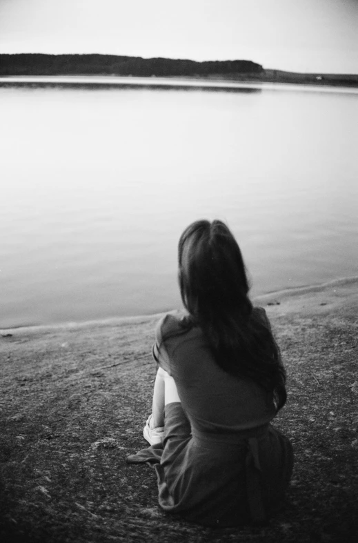 a girl sits alone on the shore of a lake