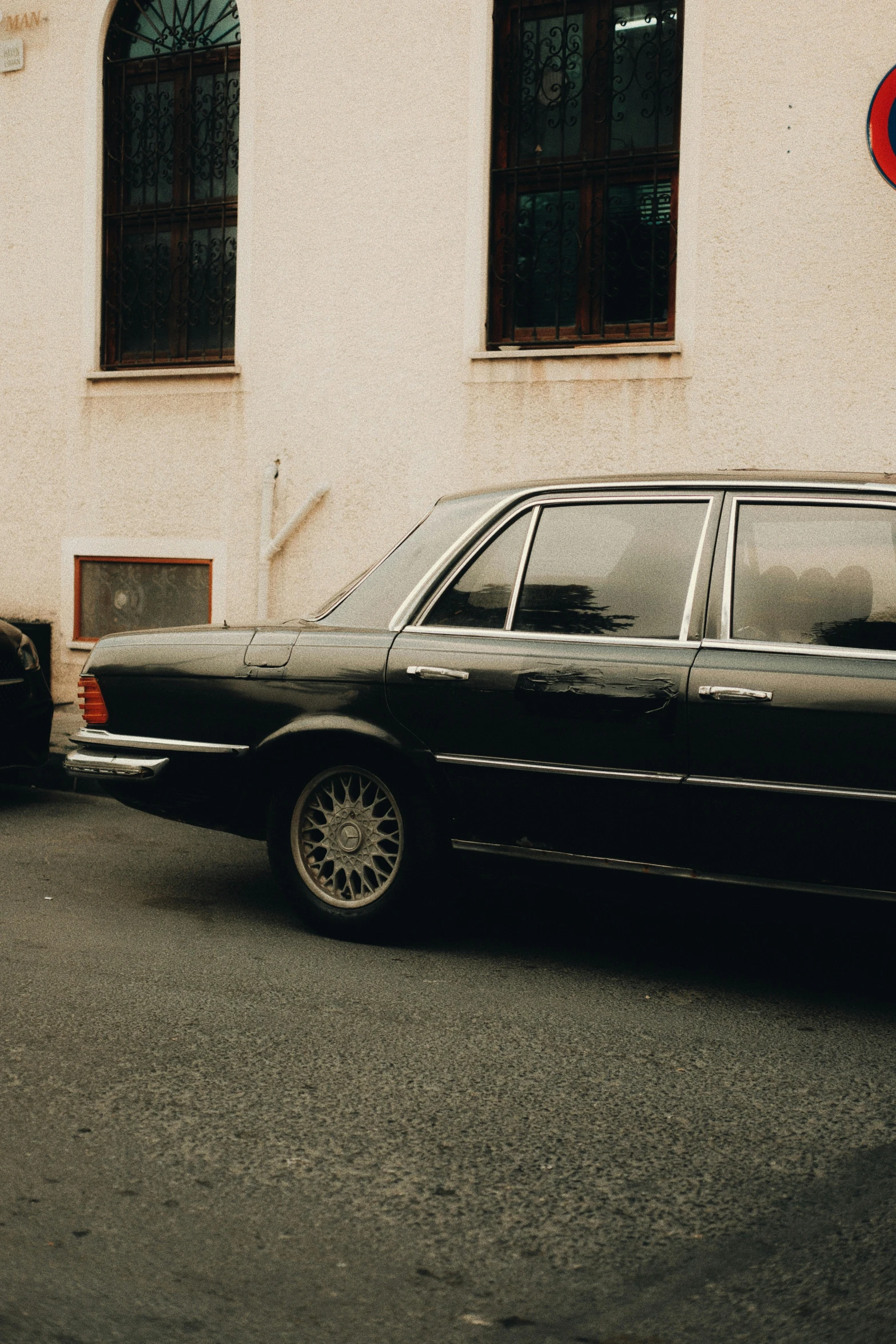 an old black sedan sits parked next to a red traffic light