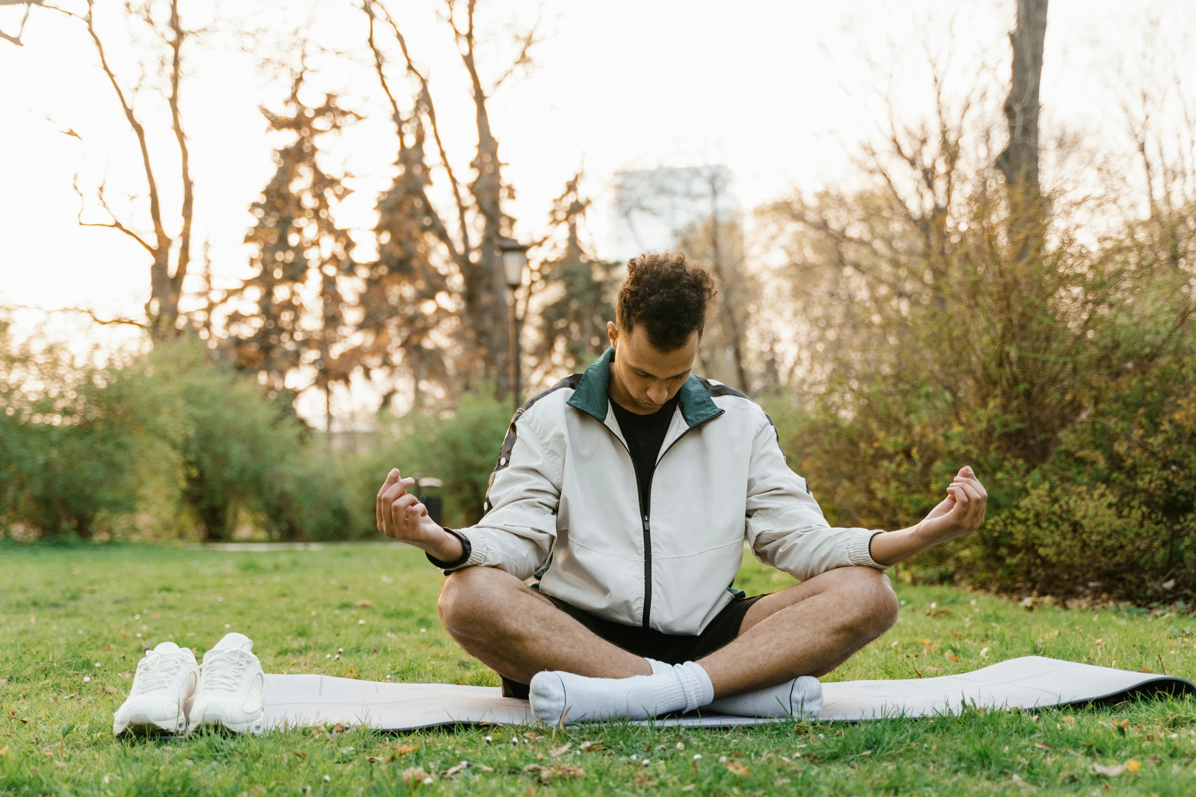 man doing yoga outdoors in the park while sitting on a mat