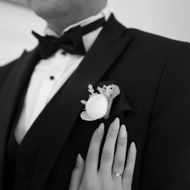 the man is wearing a tuxedo with a white flower and his hands are on the woman's lapel