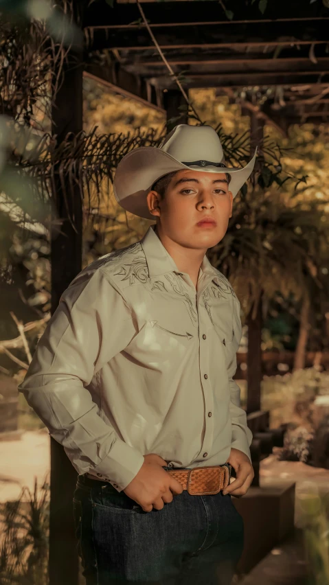 a  wearing a cowboy hat standing up with his hands in his pockets