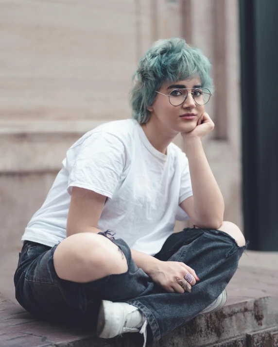 a boy with green hair wearing eyeglasses sitting on a wall