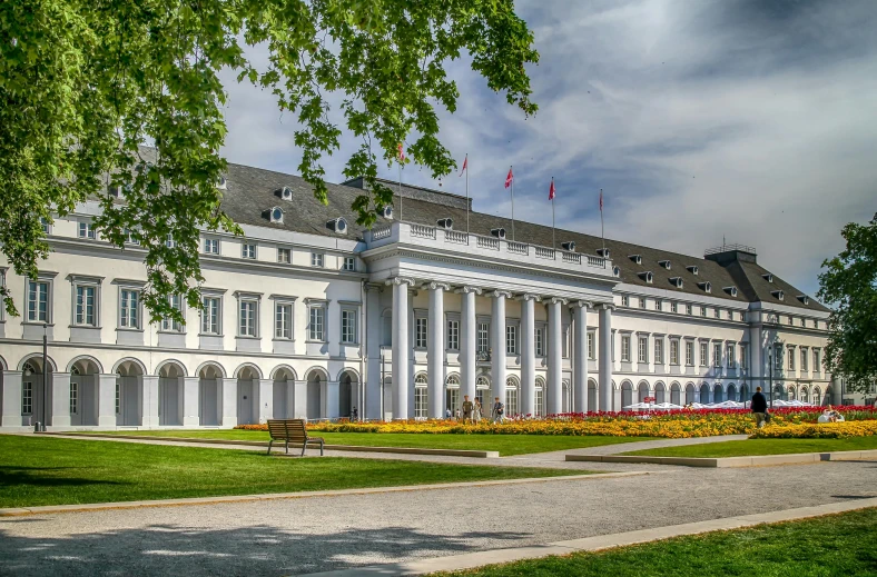 a large white building with green trees and flowers in front