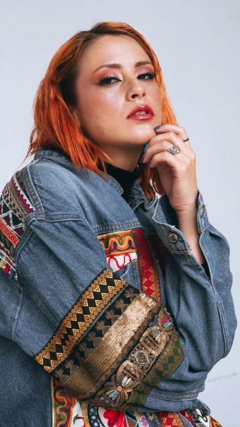 a woman with orange hair is wearing a denim jacket and is leaning against her hand