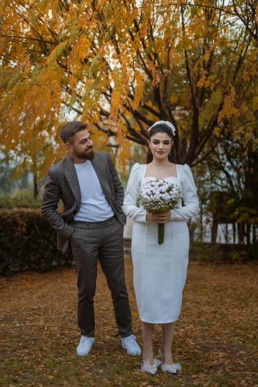 a man and woman stand under a tree in the fall