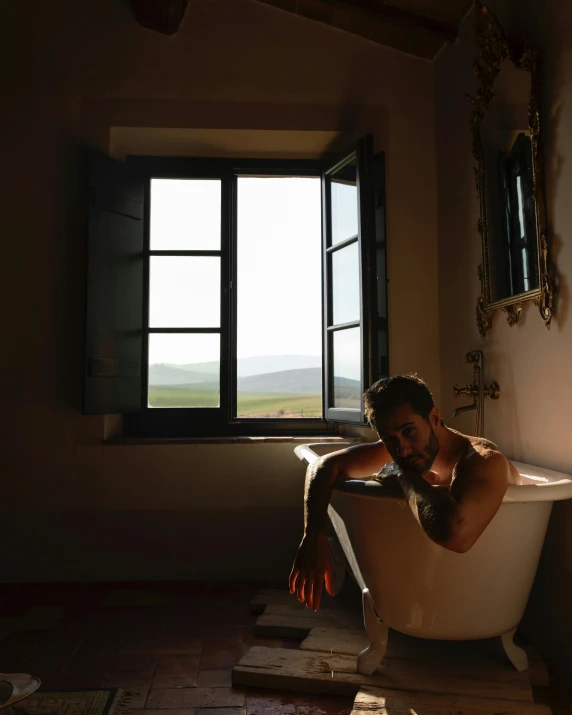 a man sitting in a bathtub, with the sun shining through a window