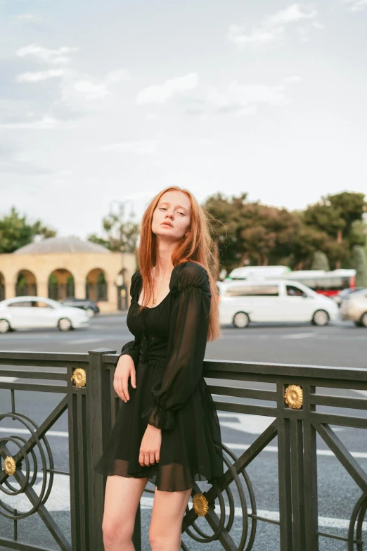 a beautiful woman in black posing by a fence