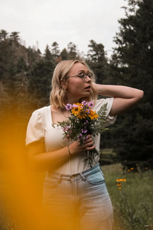 a woman holding a bouquet of wildflowers in the middle of a field