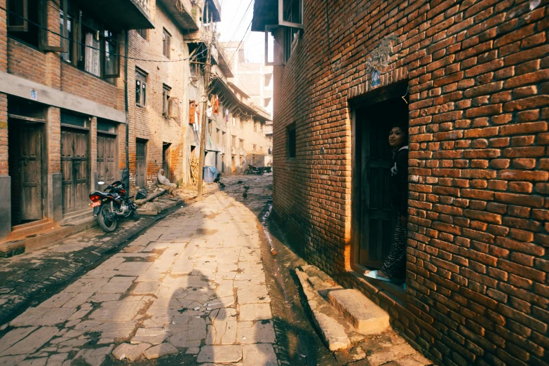 the view of a narrow alley with brick buildings, old people on bicycles, and motor scooter