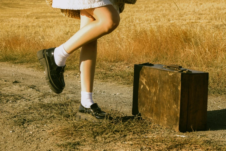 a young woman holding an umbrella standing in a field with a suitcase