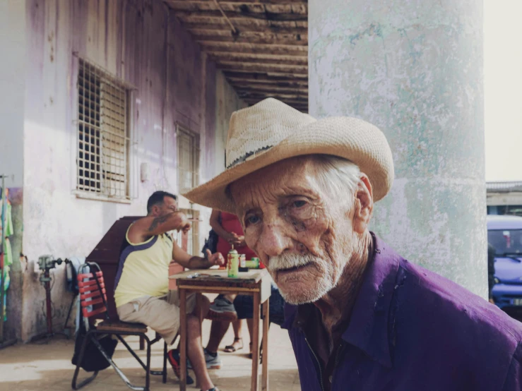 the old man is wearing a hat and sitting at an outdoor table