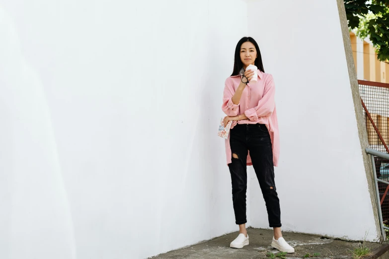 a woman stands against a wall wearing a pink sweater