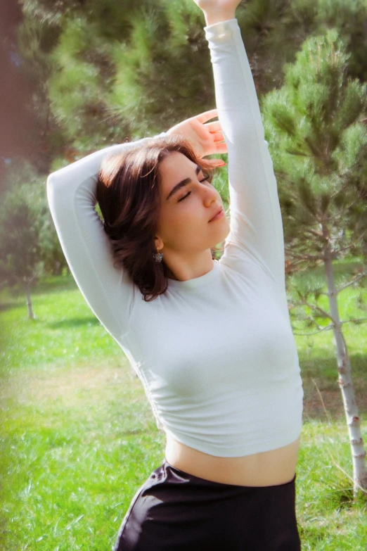 a woman stands with her arms above her head in the woods