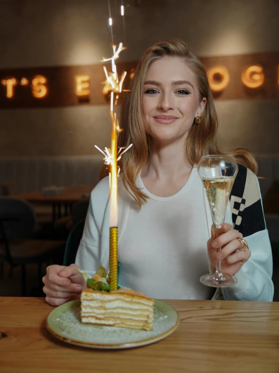 a girl holding up a sparkler over a slice of cake with wine