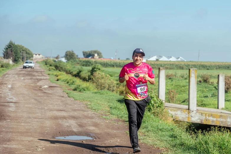 man running on dirt path next to field and wooden fence