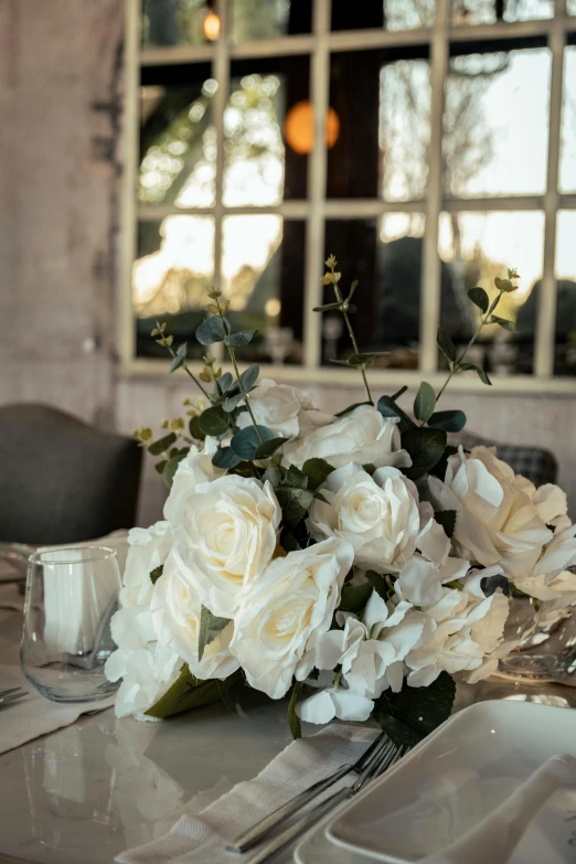 white flowers in a vase sits on a dining table