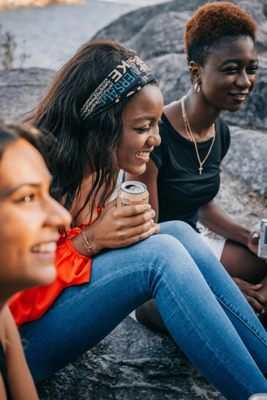 two young women laughing and drinking cans on some rocks