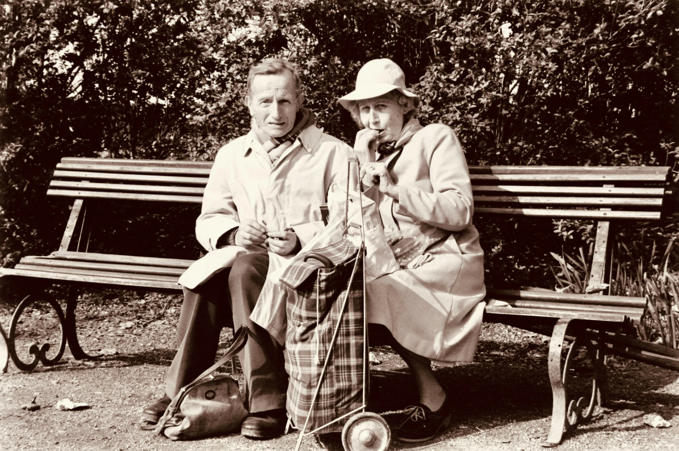 two people sitting on a bench holding their hats and looking at soing