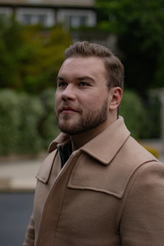 a man standing outside looking ahead with his hair tied back