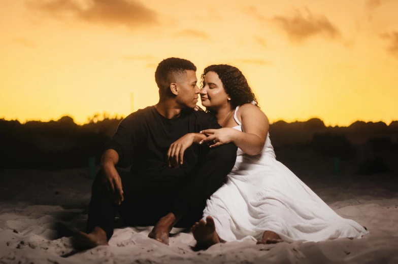 a man and woman sitting on the ground together at sunset