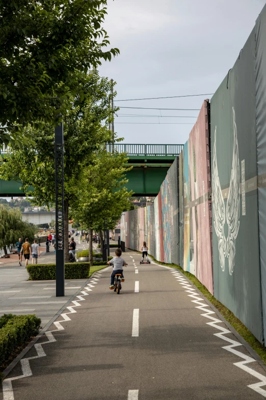 people on bikes riding in the road with a mural on the side wall