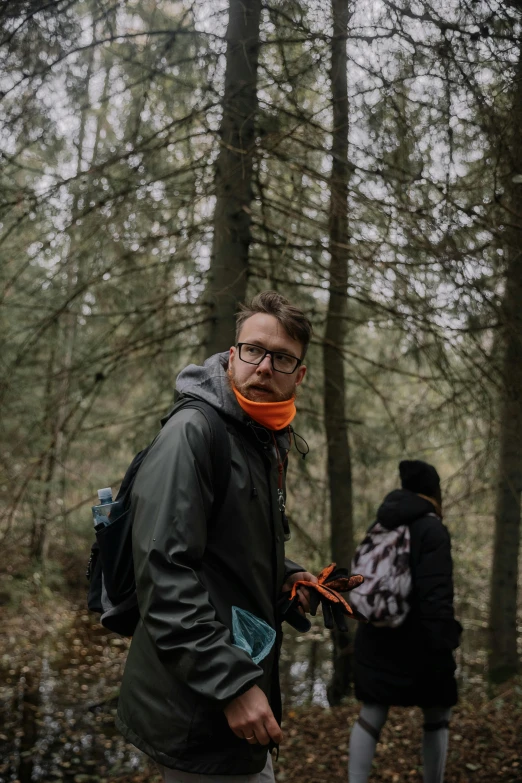 two people are walking through the woods with one man wearing an orange scarf