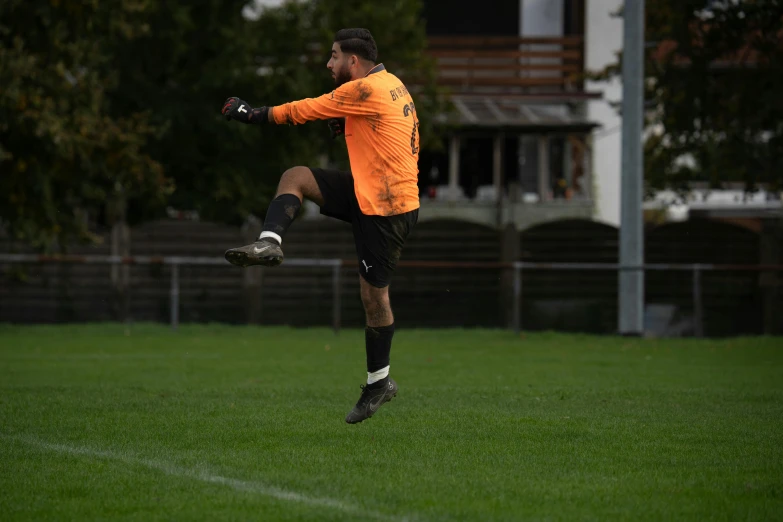 a man wearing a orange jacket kicking a soccer ball