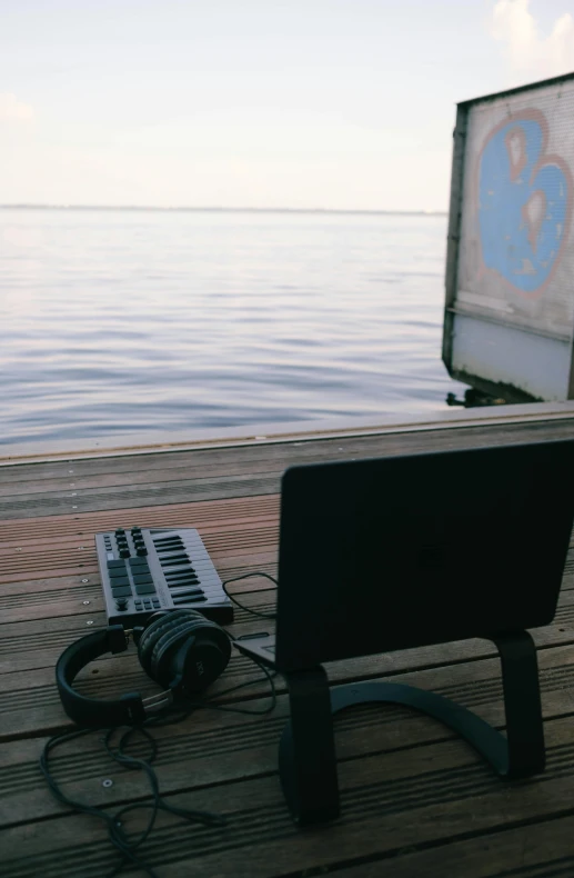 a keyboard, mouse, laptop and speaker sit on a wooden pier over water