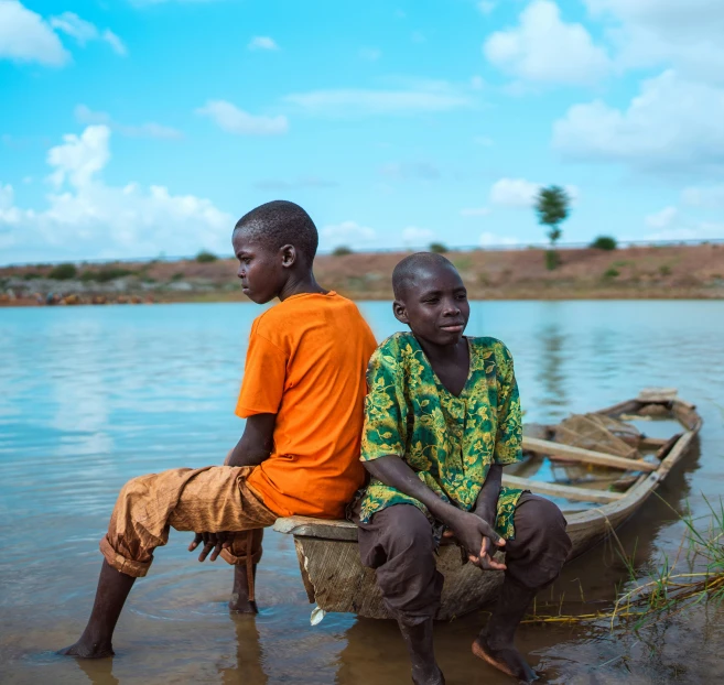 two men sit on a boat while one of them has a stick in his mouth